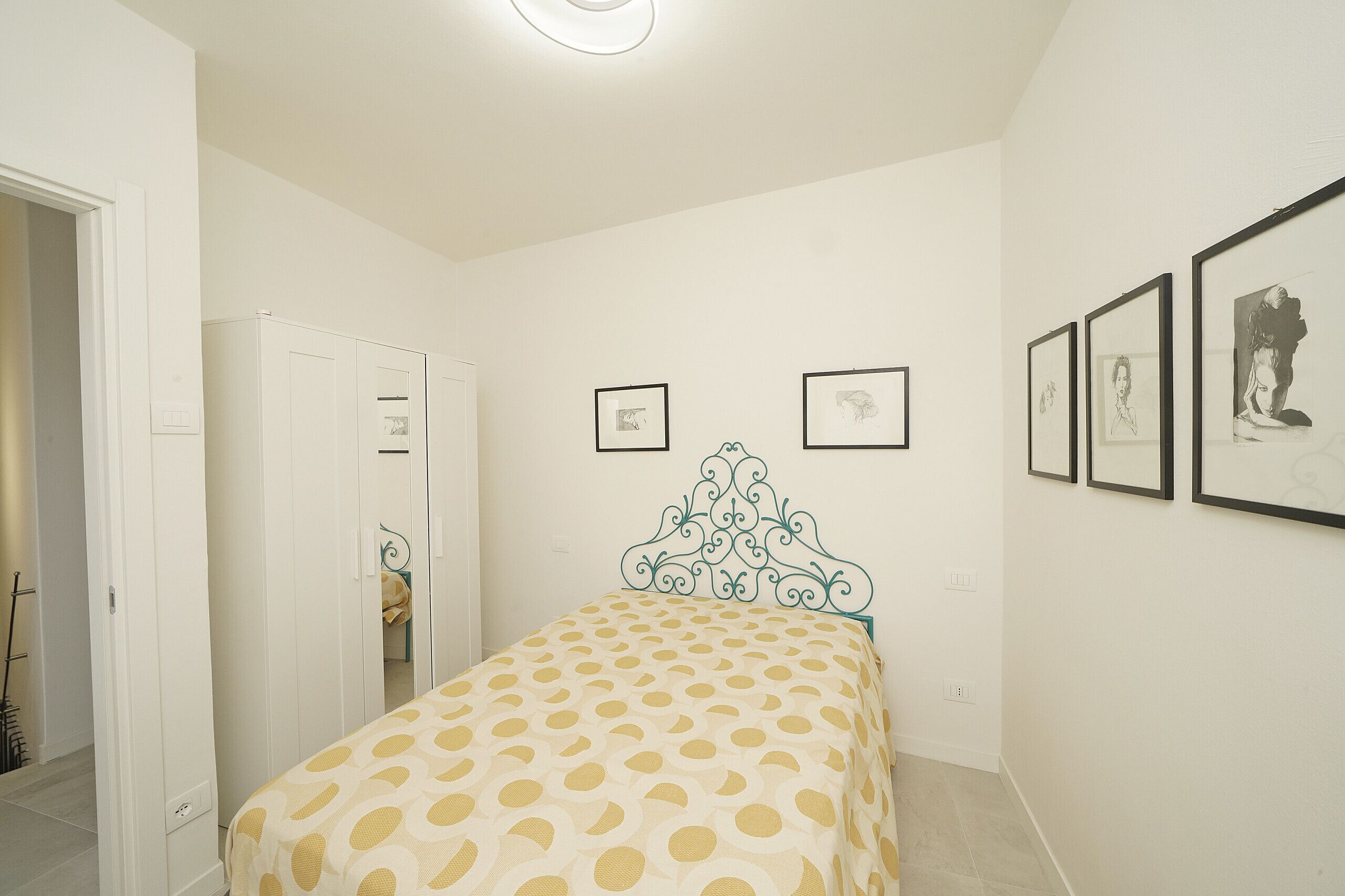 Une chambre à coucher avec un lit, une armoire et une porte. Des tableaux encadrés ornent le mur.