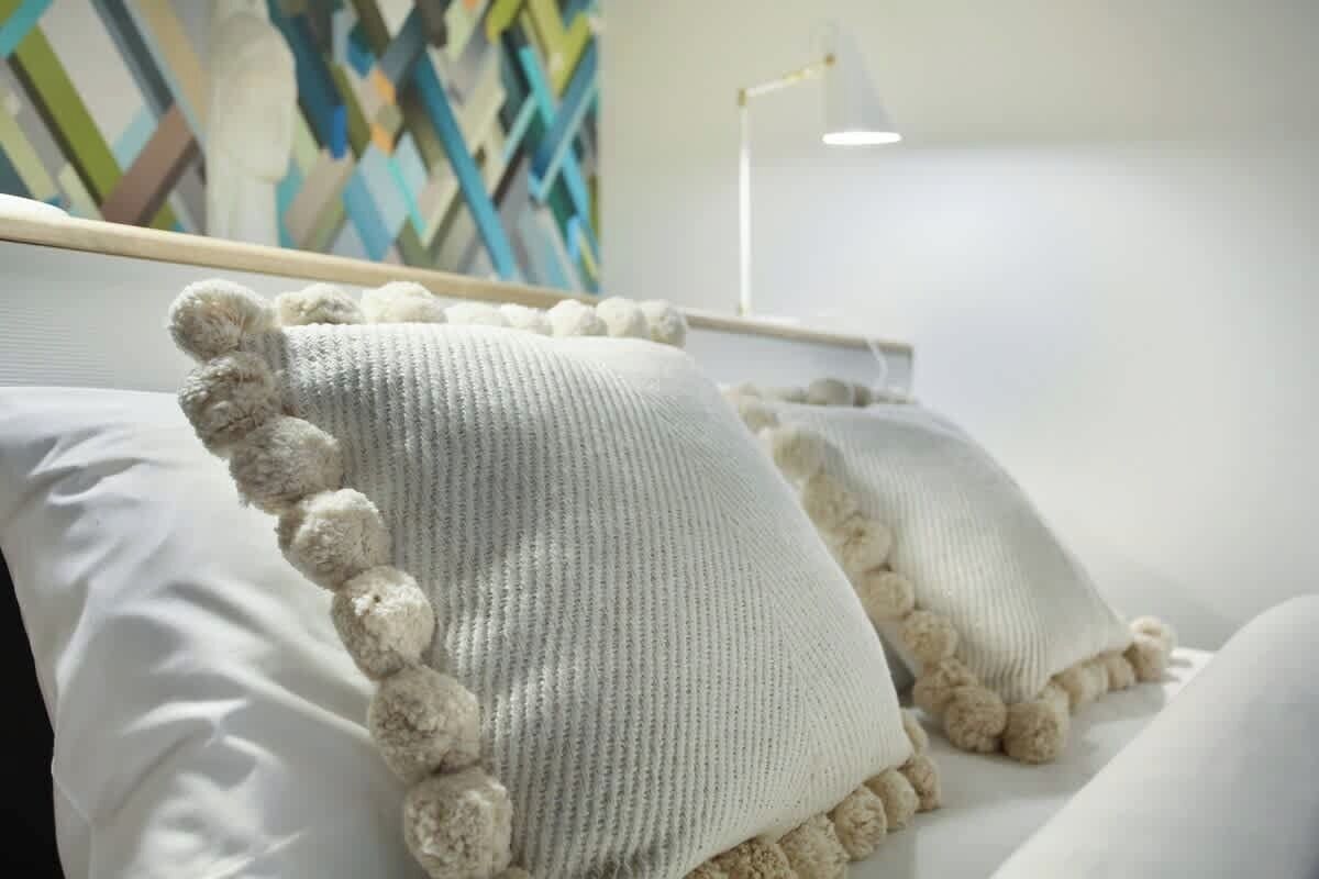 A bed with white pillows and a knitted blanket with pom-poms.