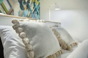 Uma cama com almofadas brancas e um cobertor de tricô com pompons.