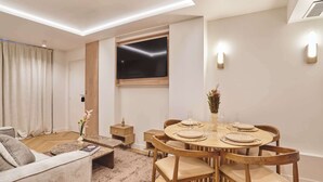 Un soggiorno moderno con un tavolo da pranzo rotondo apparecchiato per quattro persone, una TV a schermo piatto montata a parete e un’accogliente area salotto con divano e tavolino.