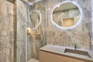 A modern bathroom with a marble wall, a round mirror, a shower with a gold fixture, and a wooden vanity. - Elegant appartement with AC - Paris Montorgueil (Paris)