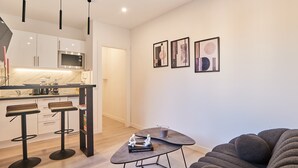 Une cuisine moderne avec des armoires blanches, un four à micro-ondes encastré et un coin bar avec des tabourets. On y trouve des œuvres d’art abstraites accrochées aux murs, ainsi qu’une petite table sur laquelle sont posés un livre et une tasse.
