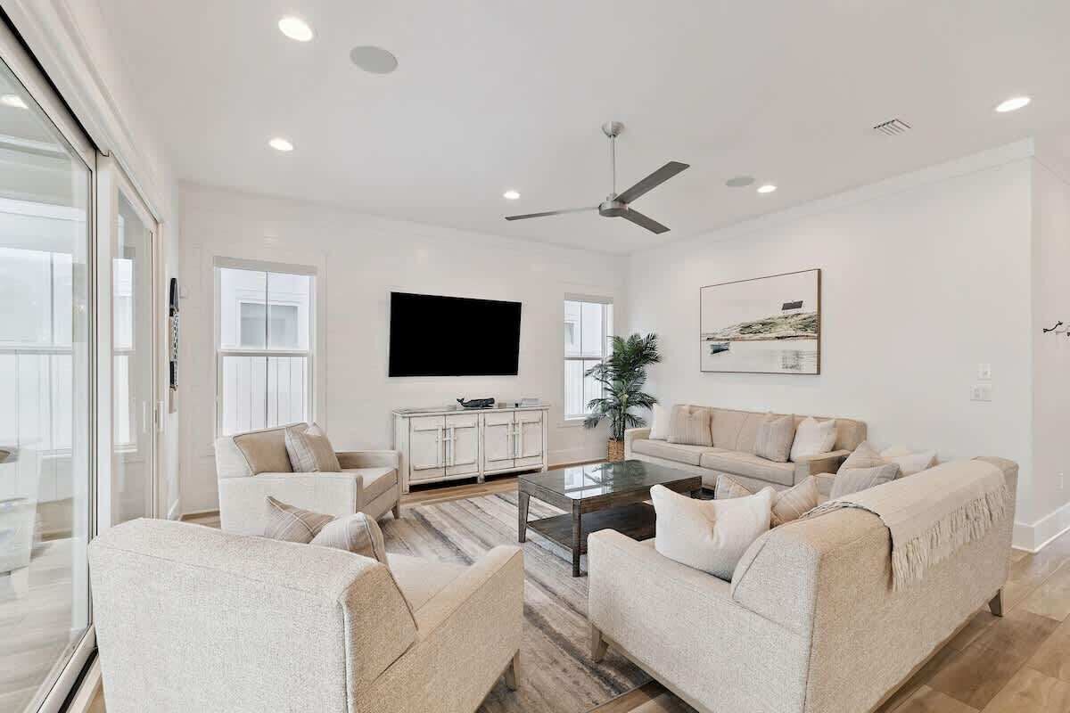 A modern living room with a flat-screen TV, a ceiling fan, and a large window.