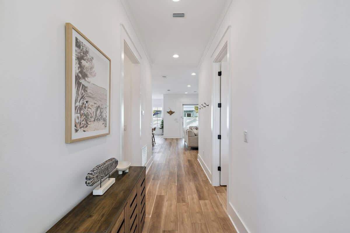 A hallway with wooden flooring, white walls, and a framed artwork on the left.