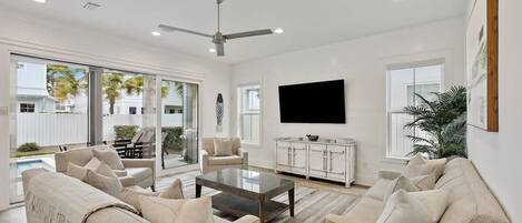 A spacious living room with a large TV, comfortable seating, and a view of the outdoors.