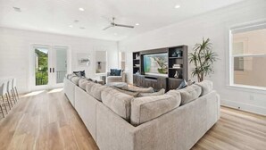 Un salon spacieux avec un grand canapé d’angle, un téléviseur à écran plat et un ventilateur de plafond.
