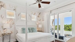 Une chambre à coucher avec un lit à baldaquin, un ventilateur de plafond et un balcon offrant une vue sur la verdure.