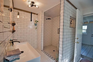 Uma casa de banho com lavatório branco, espelho e paredes revestidas a azulejos.