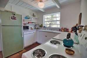 Una cocina con armarios blancos, un refrigerador verde, una estufa y un ventanal que proporciona luz natural.