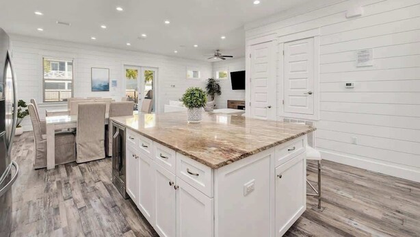 A modern kitchen with white cabinetry, a granite countertop, and a dining area with a table and chairs. - Modern 3-story Beach House W Poll and Billiard (Miramar Beach)