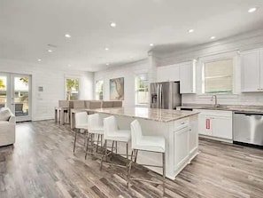 Una cocina moderna con muebles blancos, una isla central con taburetes de bar, electrodomésticos de acero inoxidable y un amplio ventanal que aporta luz natural.