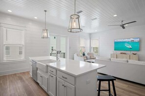 Une cuisine moderne dotée d’un grand îlot central, de meubles blancs, de luminaires suspendus et d’un ventilateur de plafond.