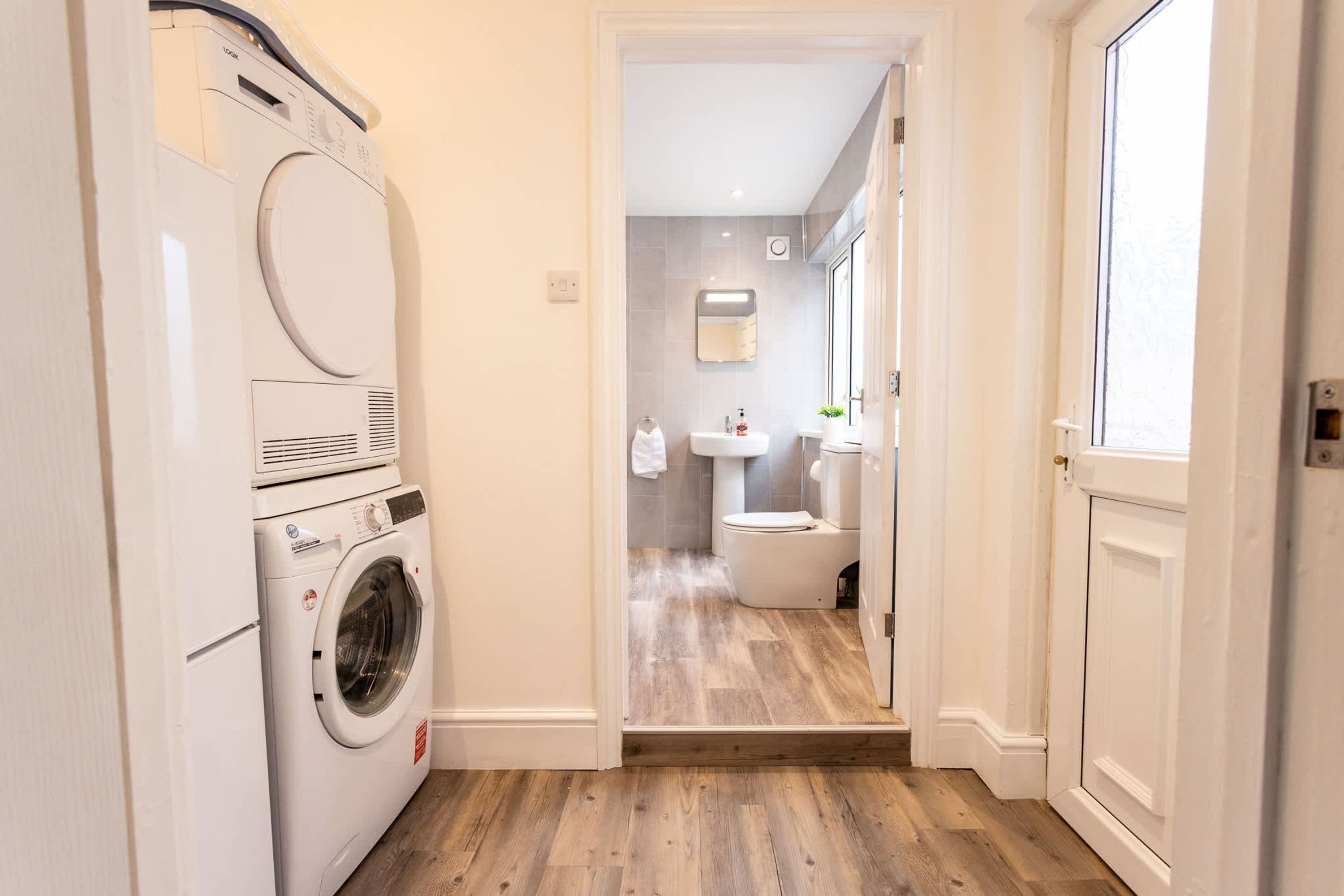 A laundry area with a washing machine and dryer, a bathroom with a toilet and sink, and a wooden floor.