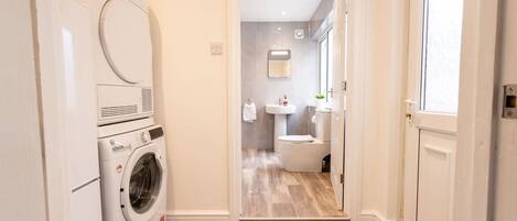 A laundry area with a washing machine and dryer, a bathroom with a toilet and sink, and a wooden floor.