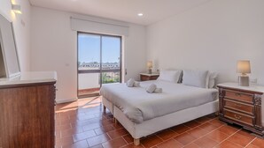 Un dormitorio con una cama grande, un aparador de madera, una mesita de noche y una ventana con vistas a edificios.
