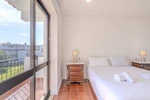 Ein Hotelzimmer mit Balkon, einem Bett mit weißer Bettwäsche, einem Nachttisch aus Holz mit Lampe und Blick auf die Stadt.
