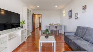 Una sala de estar moderna con televisor de pantalla plana, un sofá gris, una mesa de centro blanca y un comedor con mesa y sillas.