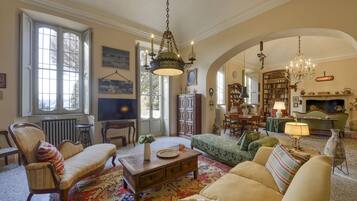 A spacious living room with a fireplace, bookshelves, and a chandelier.