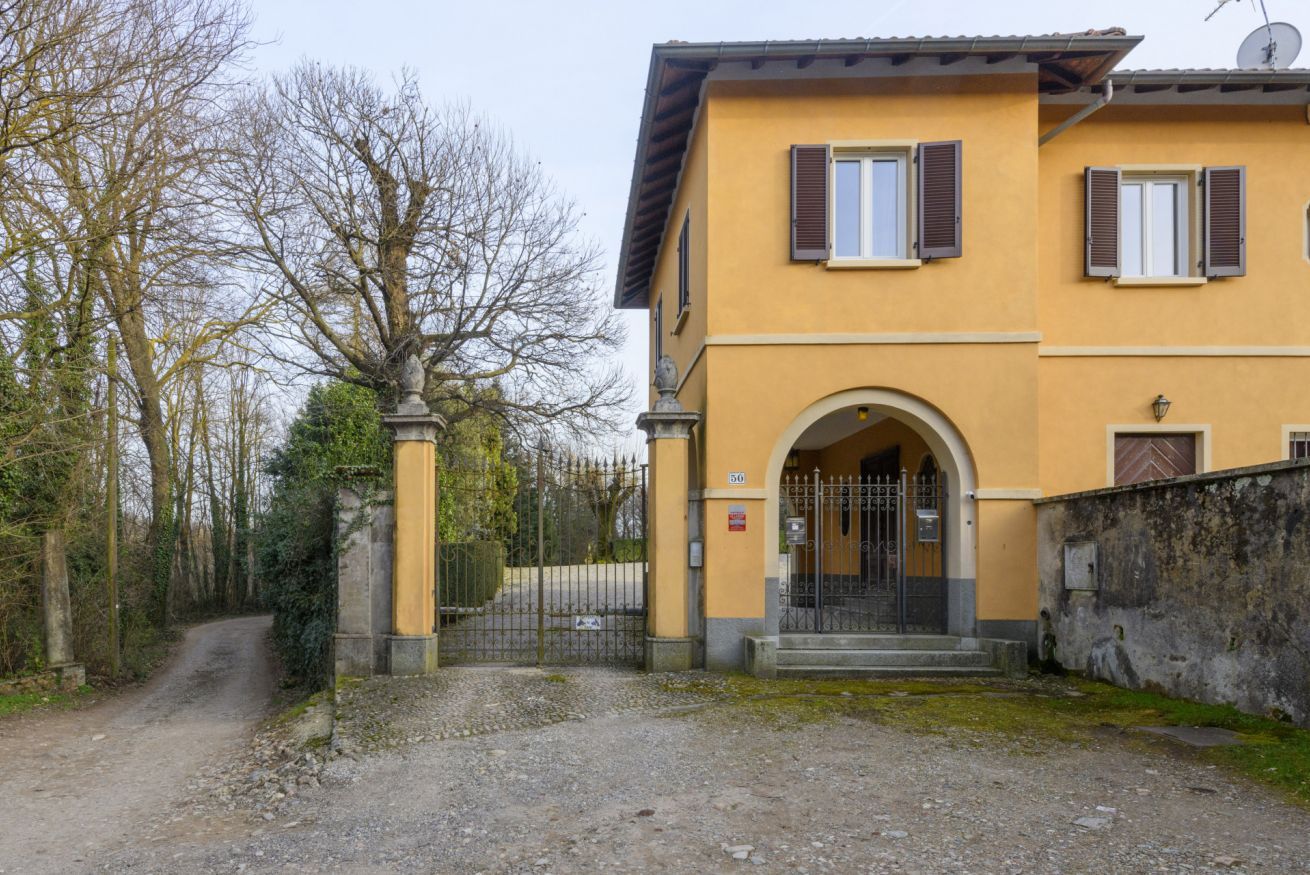 A two-story building with a yellow facade, a gated entrance, and a gravel driveway.
