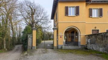 A two-story building with a yellow facade, a gated entrance, and a gravel driveway.