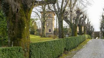 A historic building with a tower, surrounded by trees and a well-maintained hedge.