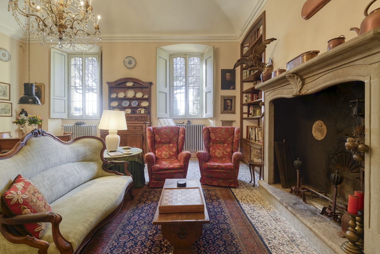 Een klassieke kamer met een bank, fauteuils, een open haard, een kroonluchter en een kamerbreed tapijt.