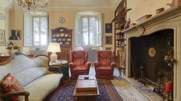Een klassieke kamer met een bank, fauteuils, een open haard, een kroonluchter en een kamerbreed tapijt.