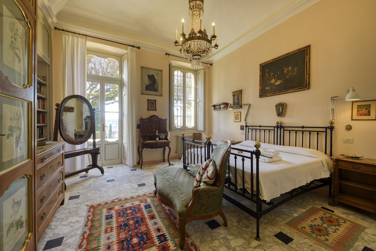 Une chambre à coucher comprenant un lit, une chaise, une commode, un miroir et un lustre.