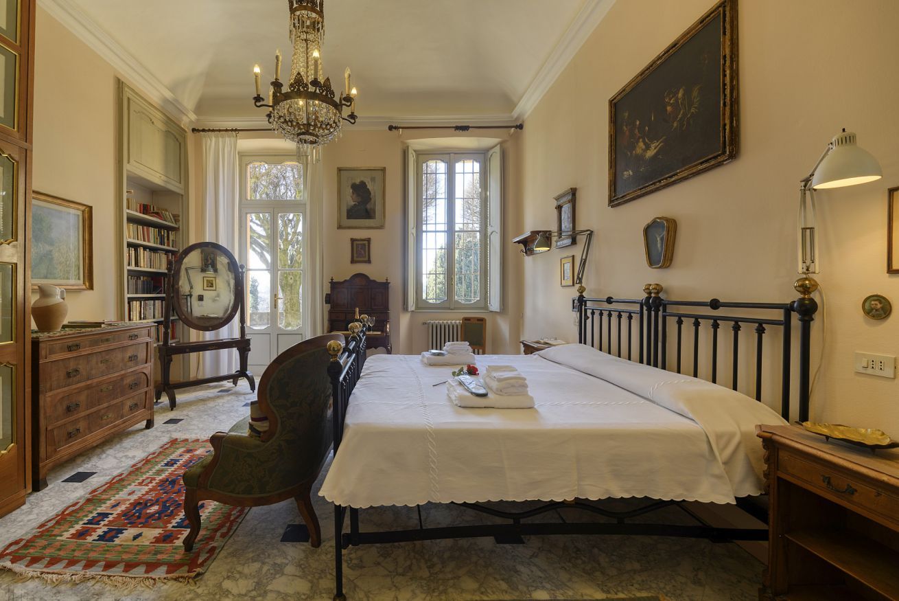 Een slaapkamer met een groot bed, een kroonluchter, een houten dressoir, een stoel en een boekenkast.