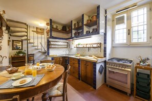Une cuisine avec des meubles en bois, une cuisinière et une table à manger dressée avec des assiettes et une carafe de jus d’orange.