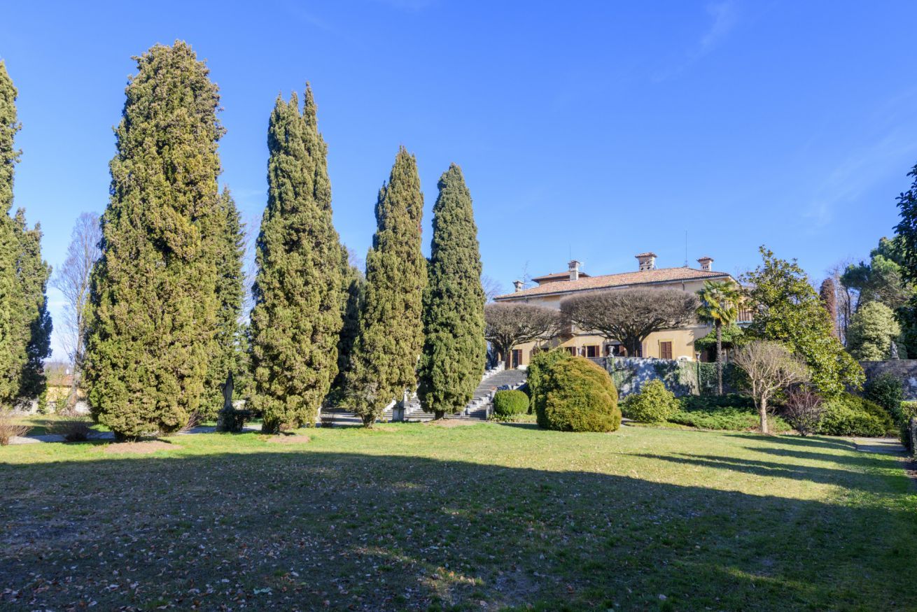 A landscaped garden with tall cypress trees, a building with a tiled roof, and a stone staircase leading to the entrance.