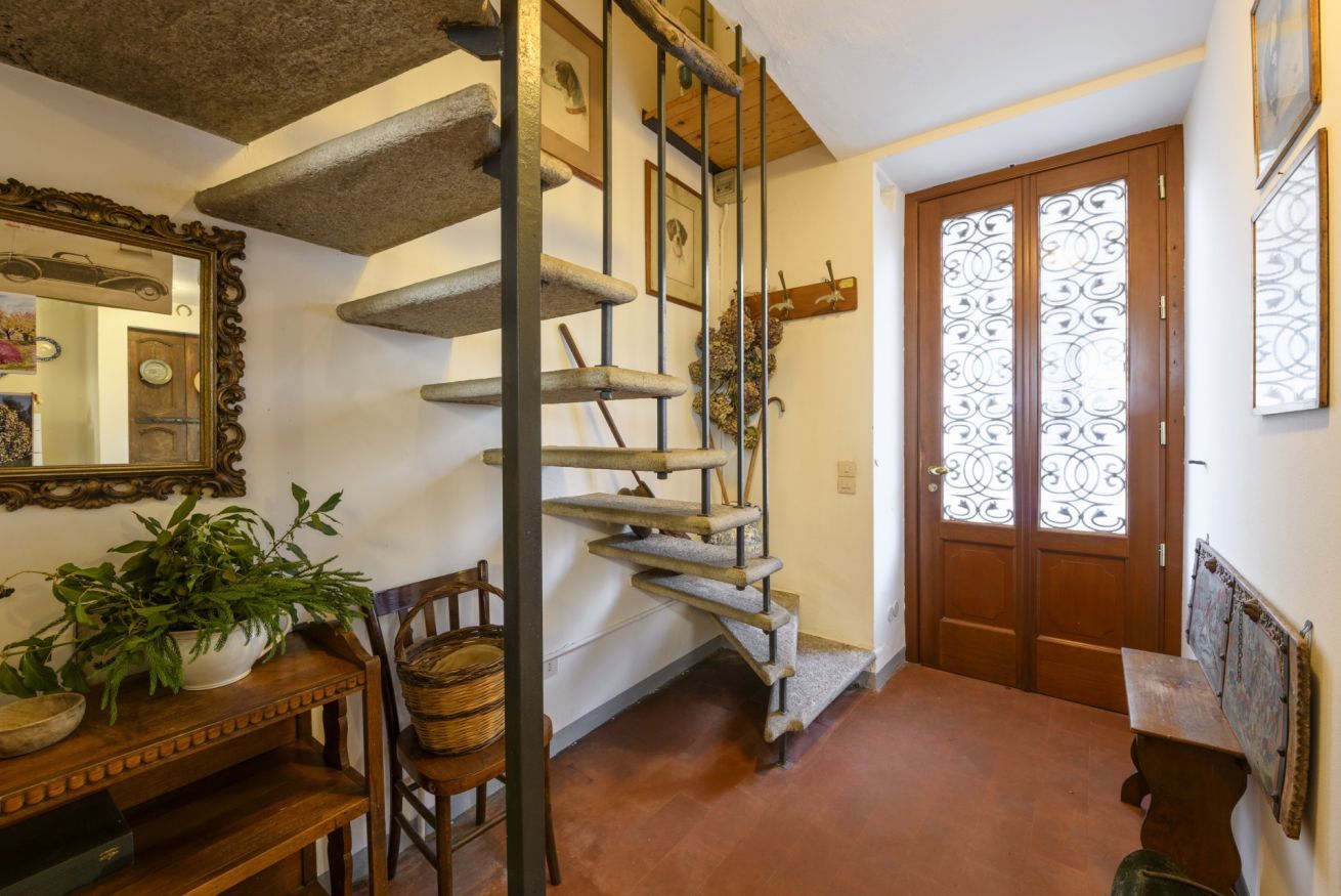A spiral staircase, a wooden door with decorative glass panels, a mirror, and a table with a plant.