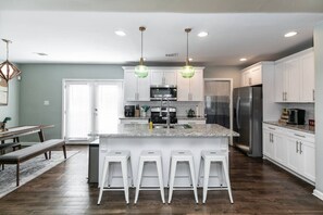 Cocina moderna con armarios blancos, encimera de granito, electrodomésticos de acero inoxidable y una isla central con taburetes de bar.