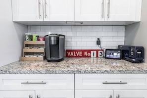 A kitchen with white cabinets, a coffee maker, a toaster, and a red sign with 'VALVE No 13' on a granite countertop. - Stylish Cottage Near Stadium, BeltLine & Downtown (Atlanta)