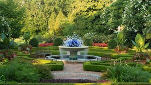 Ein formeller Garten mit einem zentralen Brunnen, ordentlich geschnittenen Hecken und verschiedenen Pflanzen.