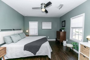 Une chambre à coucher avec un lit, un ventilateur de plafond, une commode, une fenêtre et une plante.