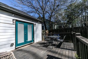 A deck with a table and chairs, a wooden fence, and a building with a teal door. - Stylish Cottage Near Stadium, BeltLine & Downtown (Atlanta)