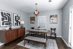 Un espace repas comprenant une table en bois, des chaises, un banc, un buffet et des œuvres d’art accrochées aux murs.