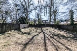 Ein Garten mit Holzzaun, Bäumen, die Schatten werfen, und einem Haus im Hintergrund.