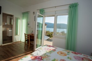 Een slaapkamer met een bed, een stoel, een bureau, een badkamer met een spiegel en een balkon met uitzicht op het water.