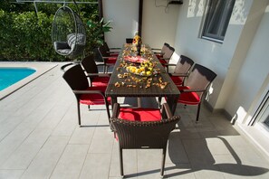 Een eettafel met stoelen, een hangstoel en een zwembad op de achtergrond.