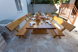 A wooden picnic table set for a meal with benches on either side, surrounded by stone flooring. - Beachfront Holiday Home With Pool Mami (Marina)