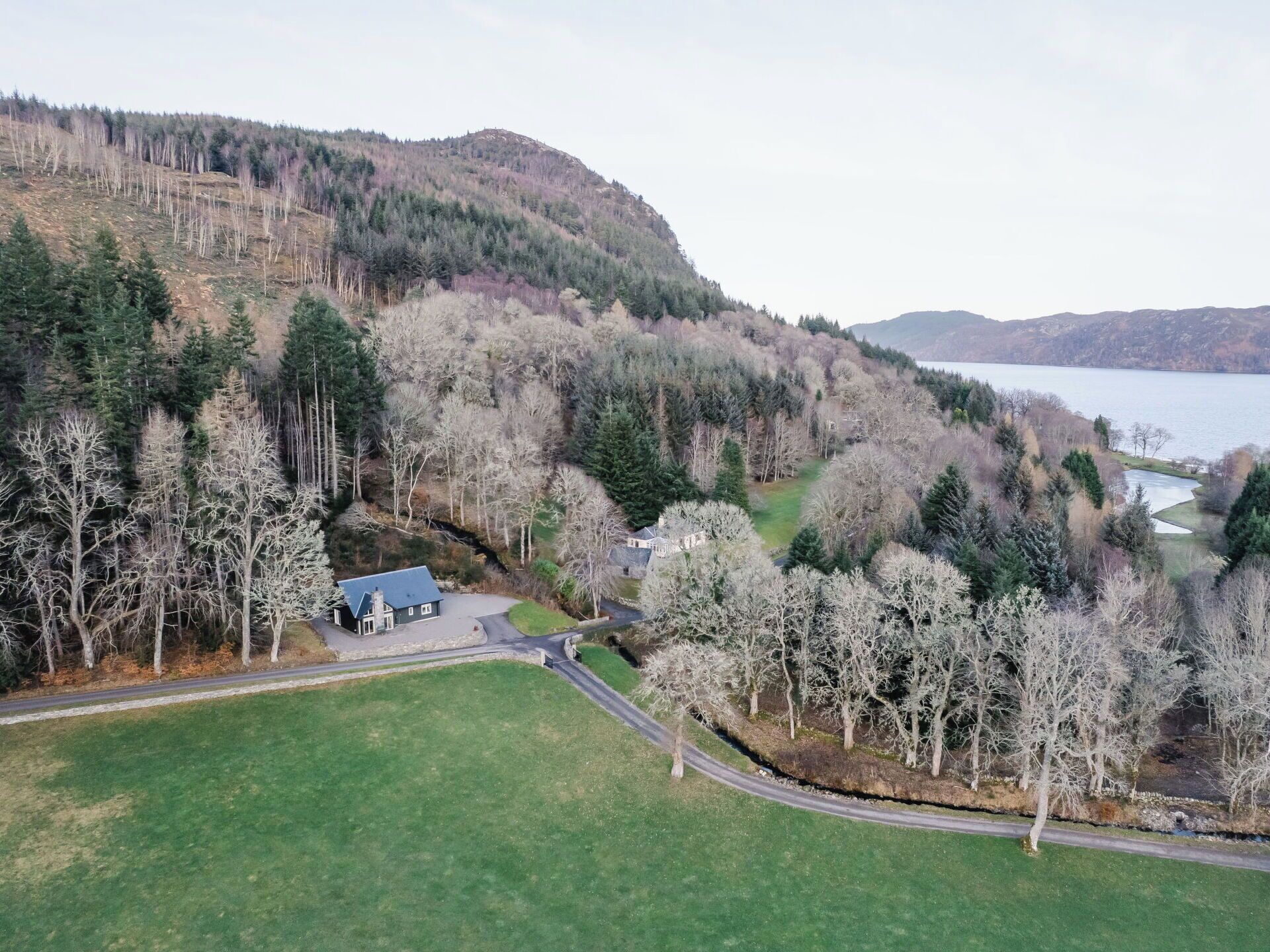 Une maison avec un toit bleu, entourée d’une pelouse verdoyante et d’une colline boisée.
