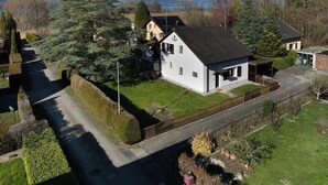A white house with a black roof, surrounded by a well-maintained garden and a paved driveway.