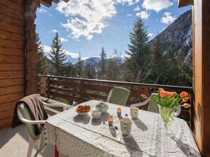 Eine Holzhütte mit einem Balkontisch, gedeckt für zwei Personen, inklusive Tischdecke, einer Schüssel mit Croissants, zwei Tassen und einem Blumenvasen mit Tulpen.