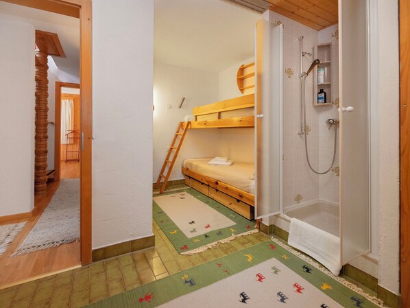 A room with a bunk bed, a shower, and a small bathroom.
