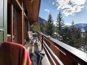 A balcony with a wooden railing, a chair, and a table with a cup.