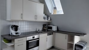Une cuisine moderne avec des meubles blancs, un four encastré, un four à micro-ondes et une machine à café.