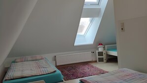 Une pièce avec un plafond en pente, un puits de lumière, deux lits équipés de tiroirs de rangement, un radiateur et une petite table avec une lampe.