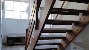 Un escalier en bois mène à une chambre dotée d’une fenêtre, d’un radiateur et d’un petit meuble de rangement.